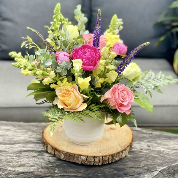 Mixed pink, yellow, and purple flowers in a white pot