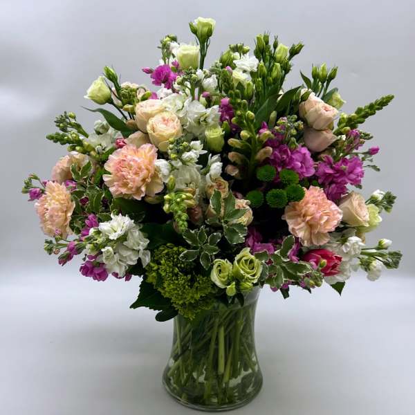 Mixed bouquet of pink, white, and green flowers in a clear glass vase