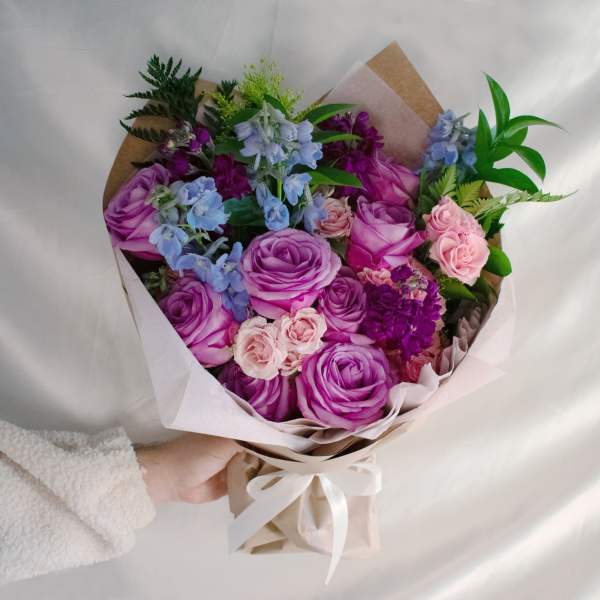 Bouquet of purple and pink roses with blue flowers wrapped in paper