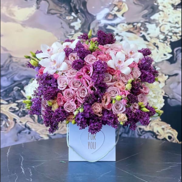 Pink and purple flower arrangement in a white gift box