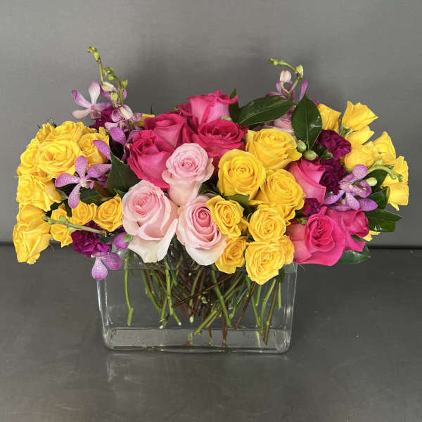 Mixed roses and orchids arranged in a clear rectangular vase