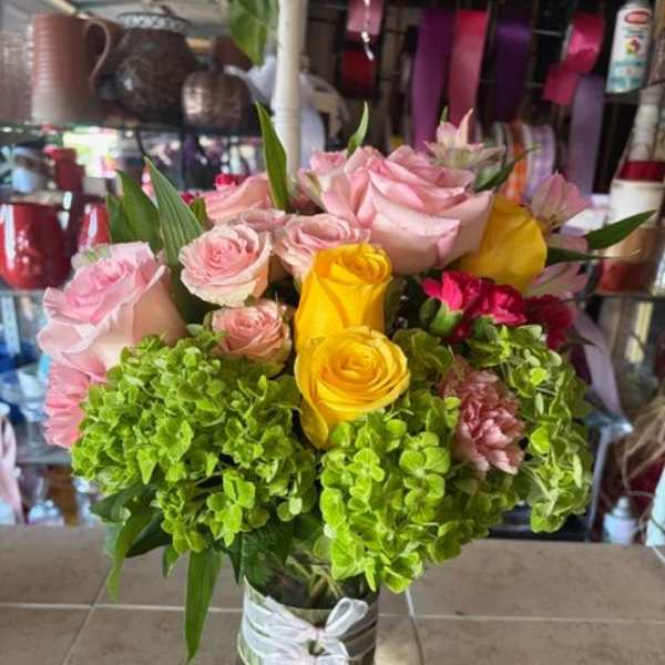 Pink and yellow roses in a clear glass vase with green hydrangeas