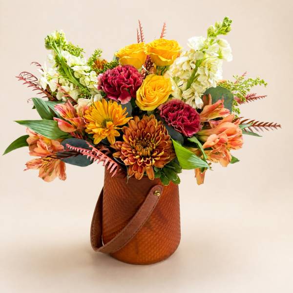 Mixed bouquet of yellow roses, carnations, chrysanthemums, and white blooms in a brown handled container