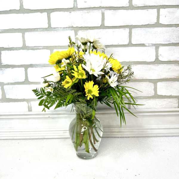 Small bouquet of yellow and white daisies arranged with greenery in a clear glass vase
