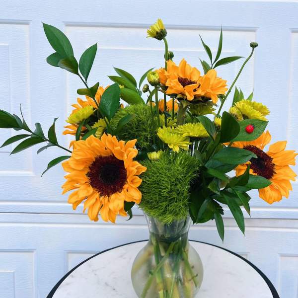 Sunflower arrangement in a clear glass vase with green filler and yellow blooms