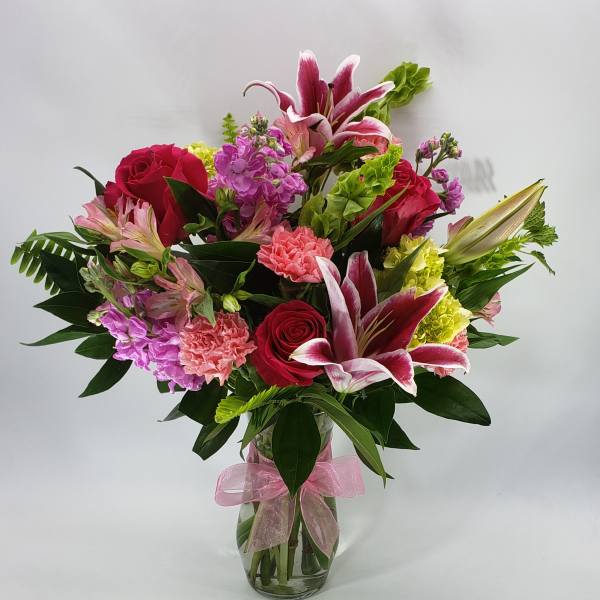 Mixed bouquet of pink and red flowers in a glass vase with a pink ribbon