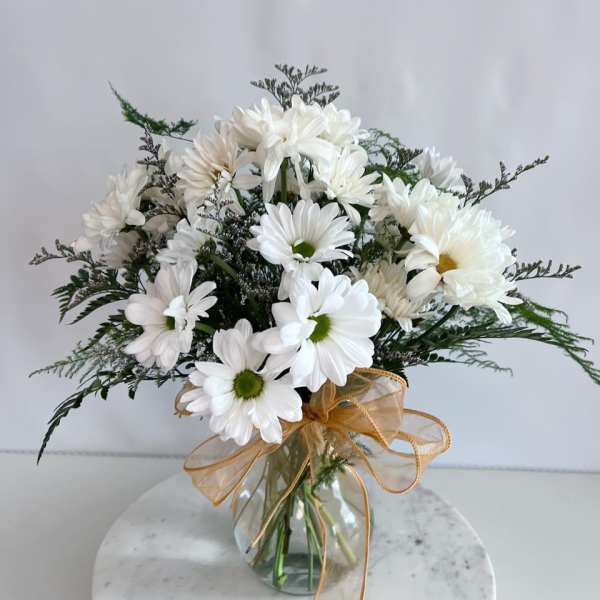 White daisy bouquet in a glass vase with a gold ribbon