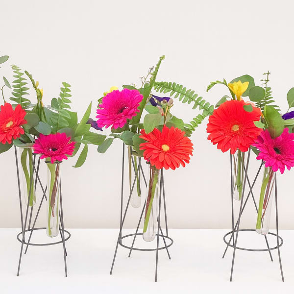 Bright gerbera daisies in slim glass vases on metal stands