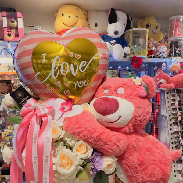 Pink teddy bear hugging a flower arrangement with a heart balloon