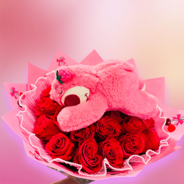 Pink teddy bear resting on a bouquet of red roses