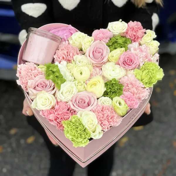 Heart-shaped pink box of pastel roses and carnations with a candle