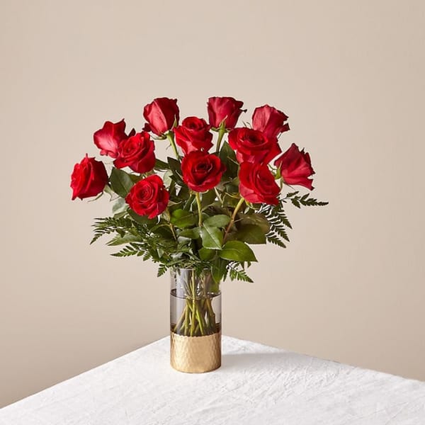 Red roses arranged in a clear glass vase with greenery