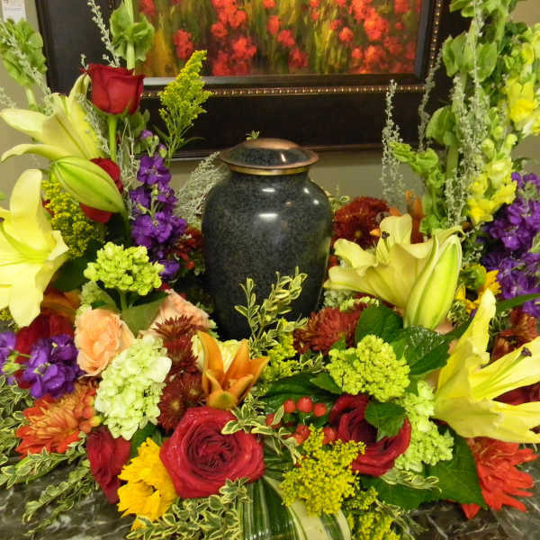 Colorful floral arrangement surrounding a dark urn on a table