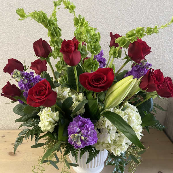 Red roses and purple blooms in a white vase