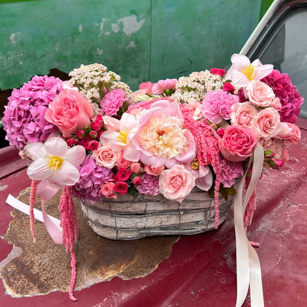 Pink floral arrangement in a woven basket with ribbon accents