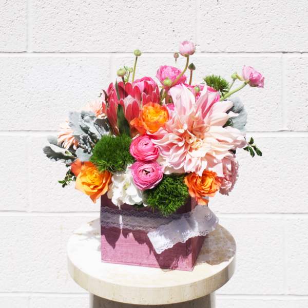 Colorful mixed flower arrangement in a pink box with lace ribbon