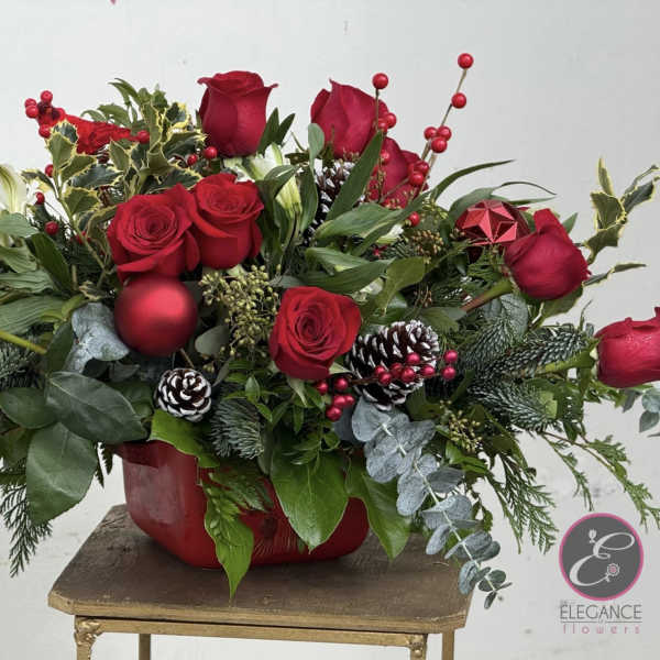 Red roses arranged in a red container with pinecones and berries