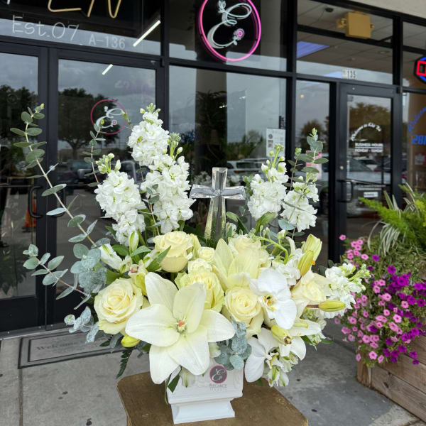 White floral arrangement with roses, lilies, and a cross in a white vase
