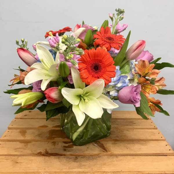 Mixed bouquet with lilies, gerbera daisies, and pastel blooms in a glass vase