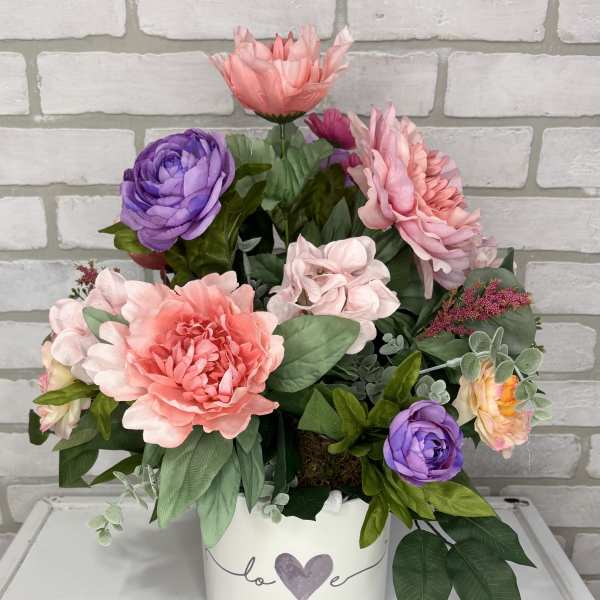 Pink and purple flowers arranged in a white heart-decorated container