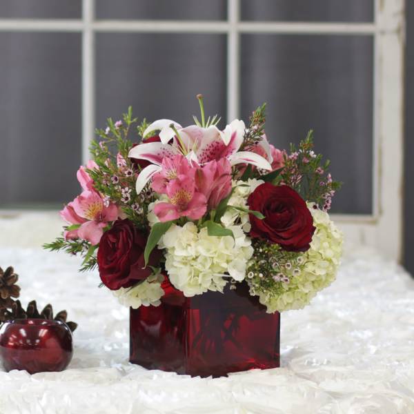 Bouquet of pink lilies, red roses, and white hydrangeas in a red glass vase