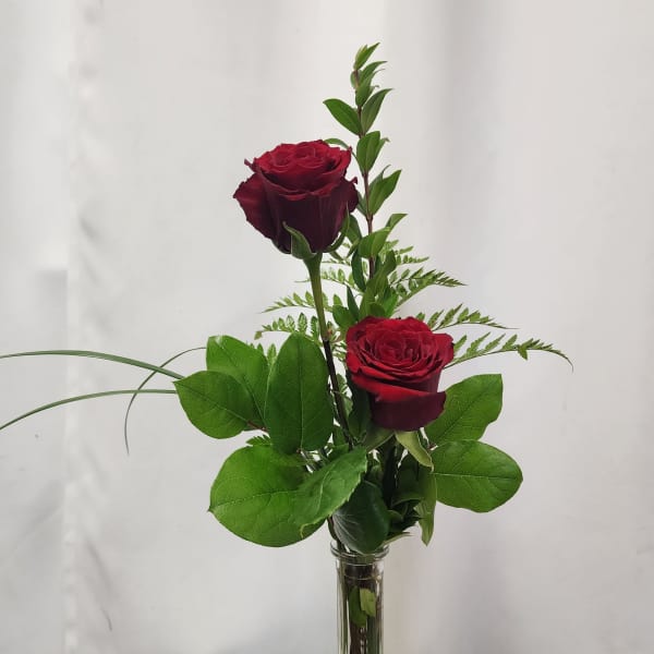 Two red roses in a clear glass vase with greenery