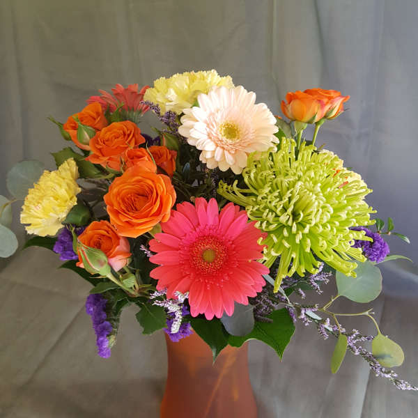 Mixed bouquet of gerbera daisies, roses, and chrysanthemums in an orange vase