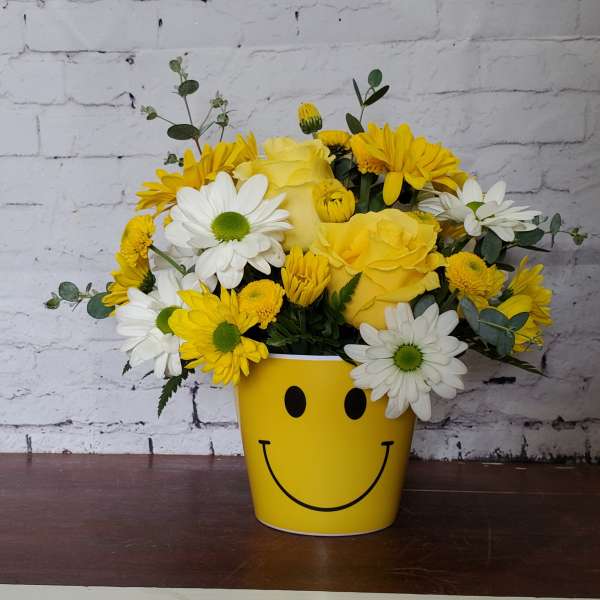 Yellow and white flower arrangement in a smiley-face pot