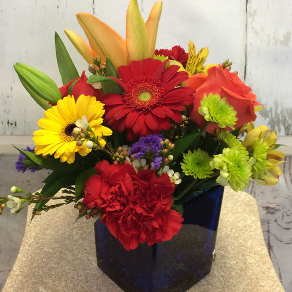 Colorful mixed bouquet in a dark blue vase with gerbera daisies, lilies, and carnations