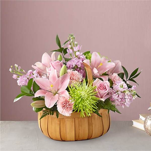 Pink lilies and roses in a wooden basket with green accents