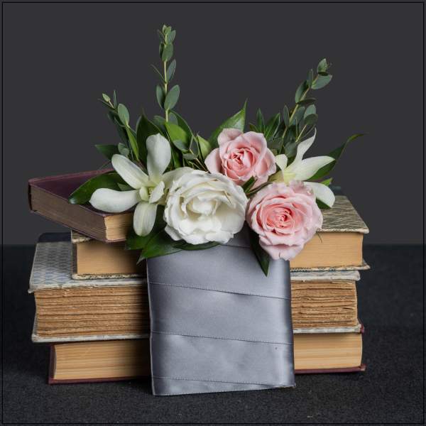 Pink and white roses with white lilies arranged over stacked books