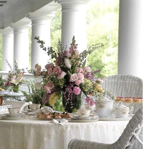 Tall pink and white floral centerpiece on a dining table with teacups