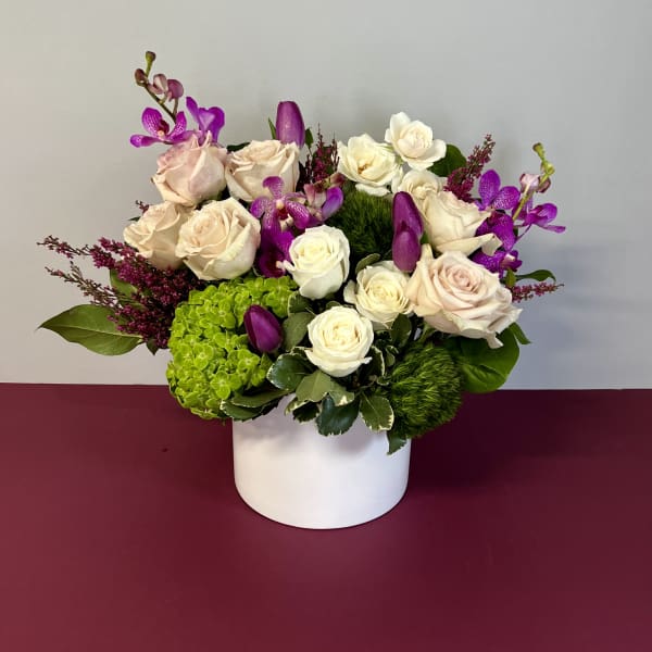 Bouquet of cream roses and purple orchids in a white vase