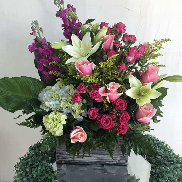 Tall arrangement of pink roses, white lilies, and hydrangeas in a rectangular gray container