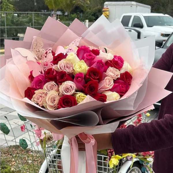 Large bouquet of pink, red, and cream roses wrapped in pastel paper