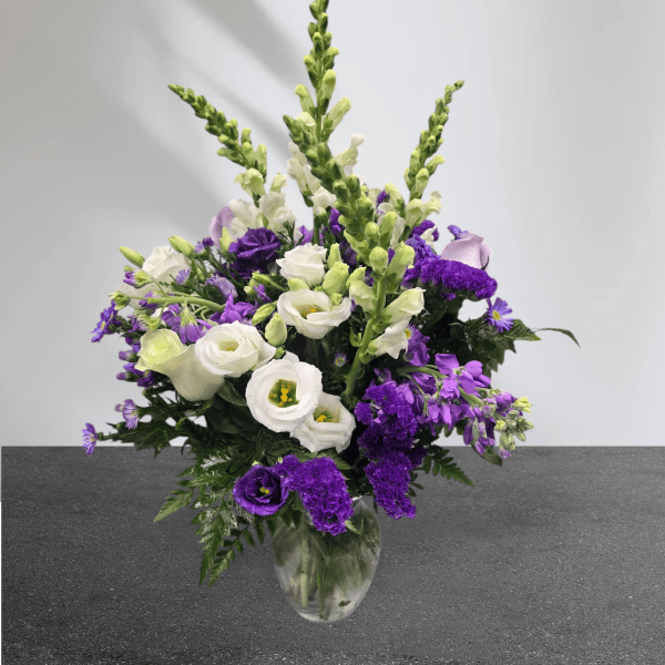 Tall arrangement of purple and white flowers in a clear glass vase