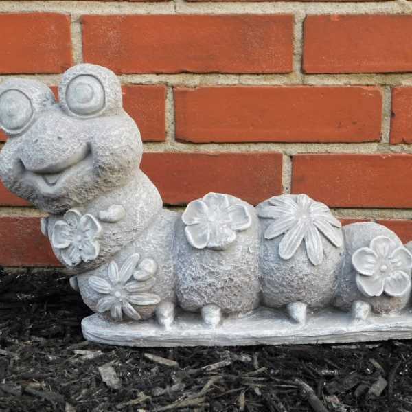 Stone caterpillar garden statue with flower decorations against a brick wall
