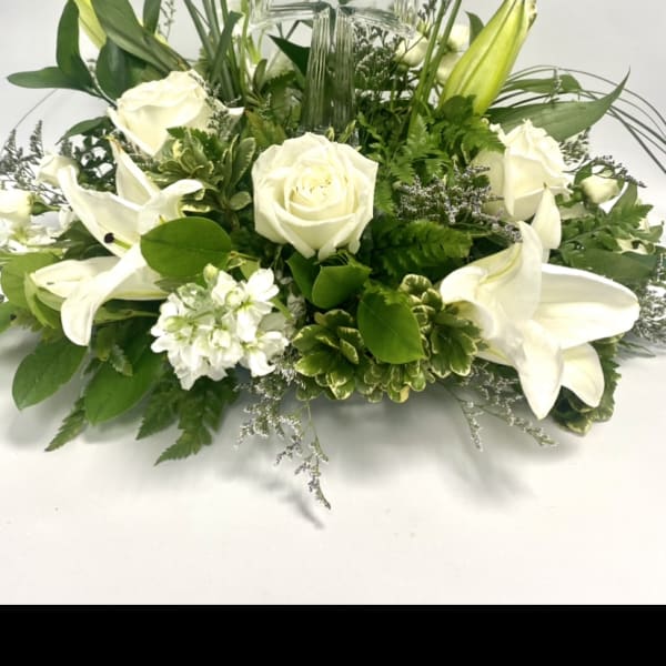 White roses and lilies arranged around a clear glass cross