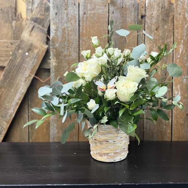 White roses in a woven basket vase with eucalyptus greenery