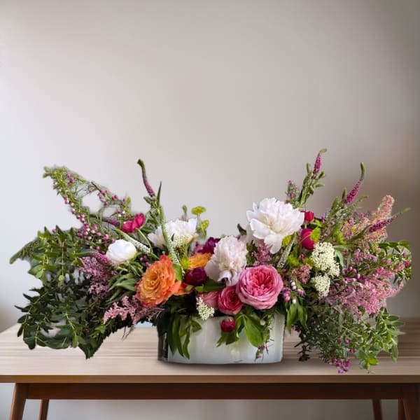 Large mixed bouquet in a low white vase with pink, white, and orange blooms