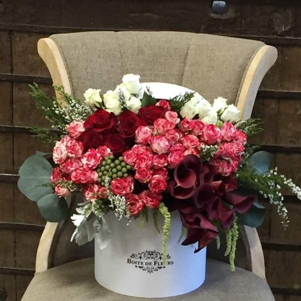 Bouquet of red and pink roses with white blooms in a white hatbox