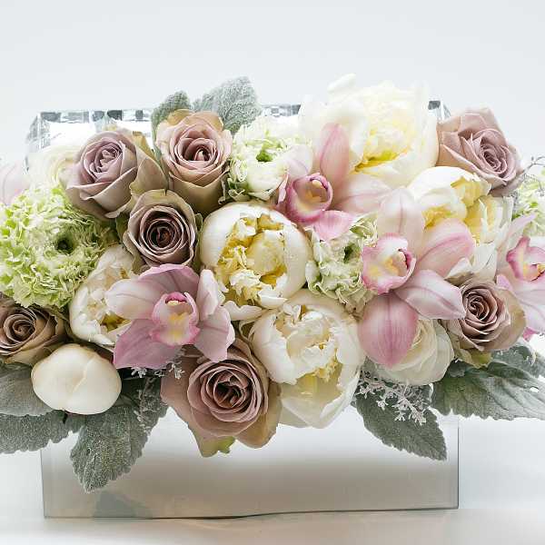 Pastel bouquet of roses, peonies, and orchids in a clear rectangular vase