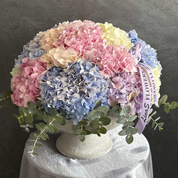 Pastel hydrangea arrangement in a white pedestal vase with ribbon