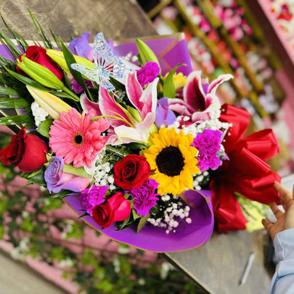 Colorful bouquet with roses, lilies, gerbera daisies, and a sunflower wrapped in purple paper