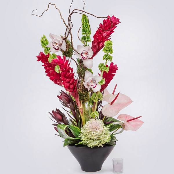 Tall tropical flower arrangement in a black vase with pink anthuriums and red blooms