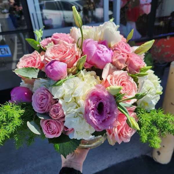 Low round arrangement of pink roses, lisianthus, and white hydrangeas in a clear glass bowl.