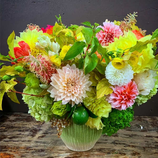 Bright mixed floral arrangement in a green vase with pink, yellow, white, and green blooms