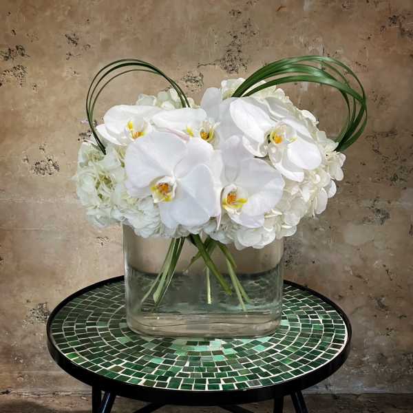 White orchids arranged in a clear glass vase with arched grass loops