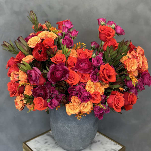 Mixed bouquet of red, orange, and purple roses in a gray vase