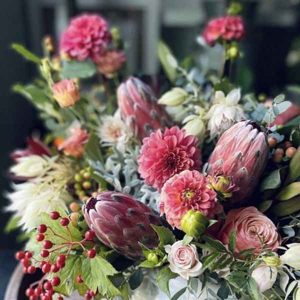 Mixed bouquet with pink blooms and protea in a white vase